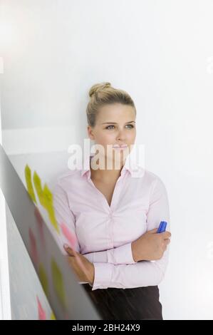 Young businesswoman, standing in office, leaning on wall, thinking Stock Photo