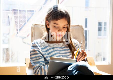 Portrait of girl sitting on armchair reading a book Stock Photo