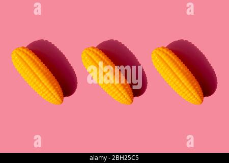 Studio shot of three plastic corn cobs against pink background Stock Photo