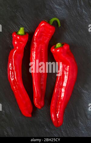 Three red chili peppers on black stone surface Stock Photo