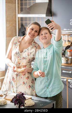 Mother and son taking selfie with smartphone in the kitchen Stock Photo