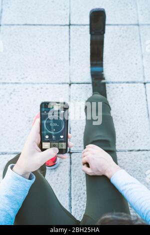 Disabled athlete with leg prosthesis having a break from exercising checking cell phone with data Stock Photo