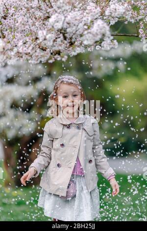 Portrait of happy little girl in a park standing under blossoming Japanese cherry tree Stock Photo