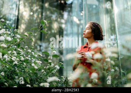 Portrait of pensive young woman standing in urban garden looking up