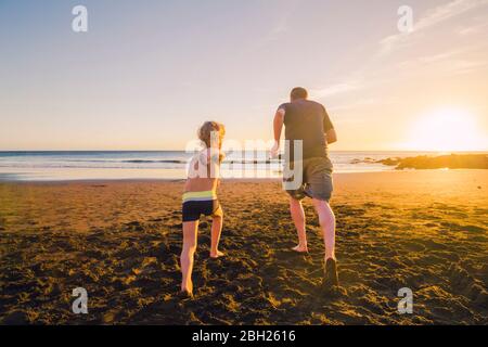 Father and son running on the beach, rear view