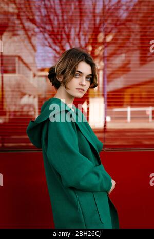 Young woman wearing green coat in front of a red glass pane Stock Photo