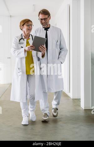 Two doctors waking along hallway using tablet Stock Photo
