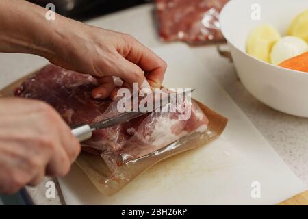 Hands of woman in process of opening vacuum package of meat on a white plastic cutting board Stock Photo