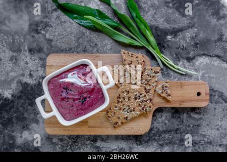 Cutting board, bowl of beetroot dip, crispbread and fresh ramson Stock Photo
