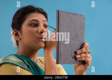 Kathak dancer applying eyeliner on her eyes. Stock Photo