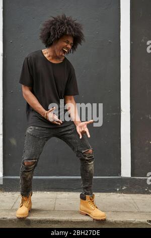 Young black man with afro singing and dancing in front of grey wall Stock Photo