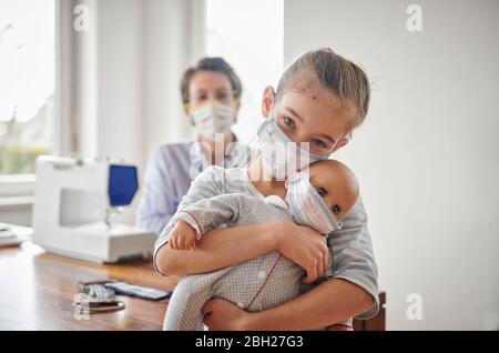 Little girl and her doll, wearing face masks, her mother has made for them Stock Photo