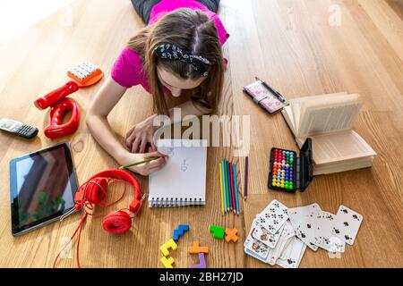 Girl lying on floor with play equipment, drawing on pad Stock Photo
