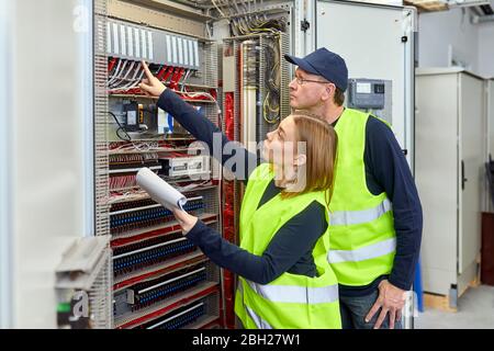 Two electricians with plan looking at fuse box Stock Photo