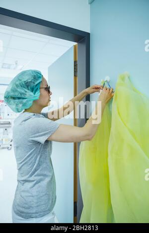 Doctor taking personal protective equipment from hook in hospital Stock Photo
