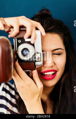 Portrait of young woman with red lips taking picture of viewer with camera