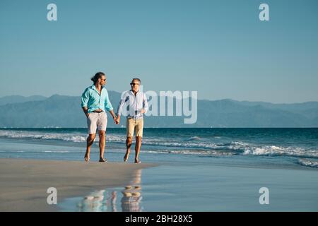 2 gay men walking hand in hand at a remote beach in Mexico. Stock Photo