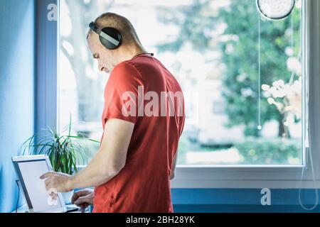 Man with headphones using digital tablet near window at home Stock Photo