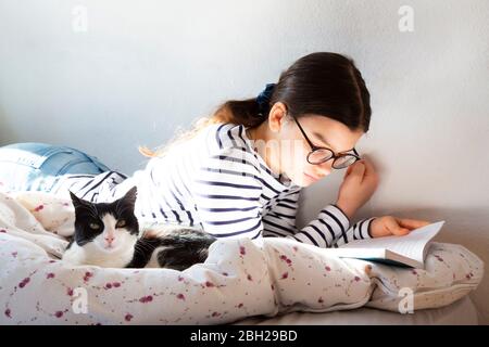 Girl lying on bed with cat reading a book Stock Photo