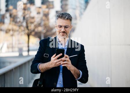 Smiling gray-haired businessman in the city using cell phone Stock Photo