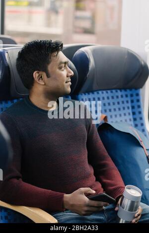 Man holding reusable cup and smartphone in the train Stock Photo