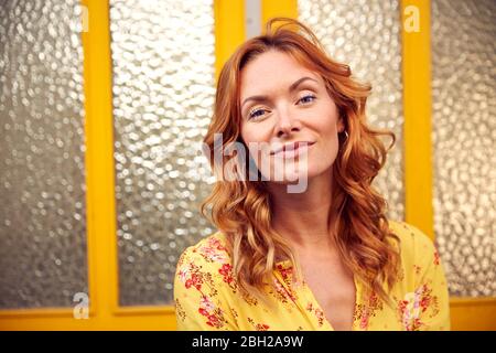 Portrait of red-haired happy woman in front of door, smiling at camera Stock Photo