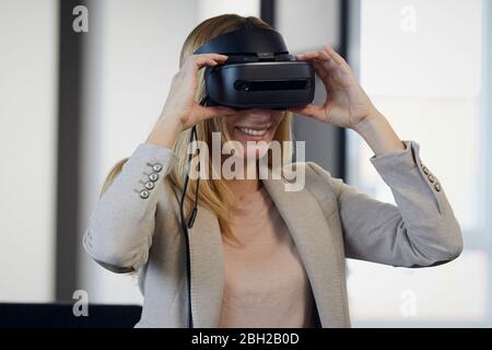 Smiling businesswoman wearing VR glasses in office Stock Photo