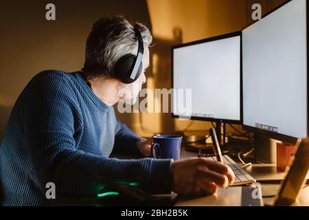 Mature man sitting at desk at home working with graphics tablet and computer Stock Photo