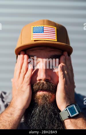 Bearded man wearing baseball cap with American flag wiping off sweat from his face Stock Photo