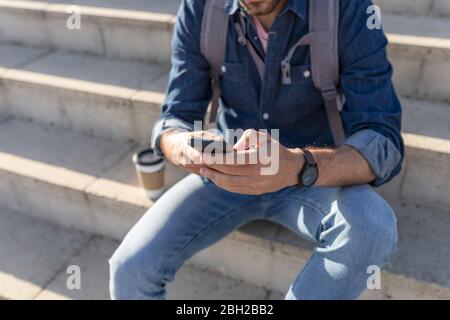 Crop view of man sitting on stairs using smartphone Stock Photo