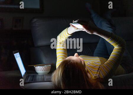 Young woman lying on the couch at home using smartphone Stock Photo