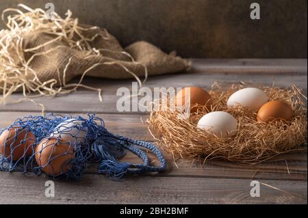 Brown and white chicken eggs in a straw nest on wooden background. Next to eco string bag with eggs. Rustic style Stock Photo