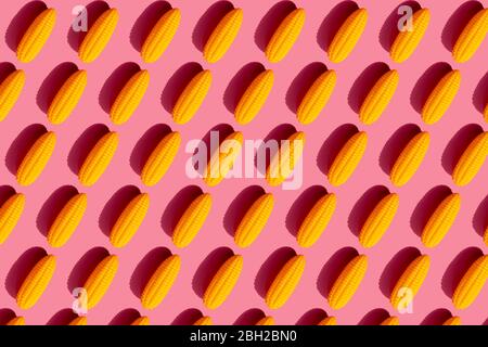 Pattern of yellow plastic corn cobs against pink background Stock Photo