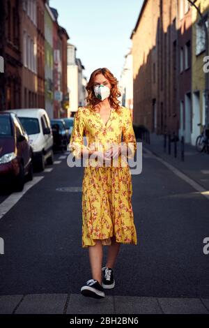 Red-haired woman wearing a FFP2 face mask and walking on empty road Stock Photo