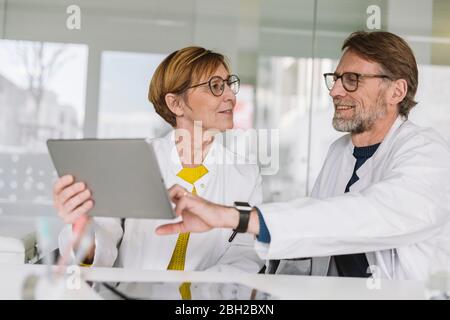 Two doctors sitting at desk using tablet Stock Photo