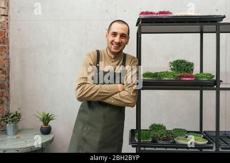 Portrait of happy man leaning against shelf with microgreens Stock Photo