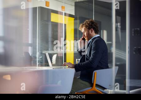 Businessman sitting at desk in office using laptop and smartphone Stock Photo