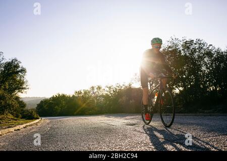 Athlete riding bicycle on country road at sunset Stock Photo