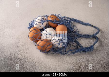 Brown and white chicken eggs in string bag on a light textured background. Copy space Stock Photo