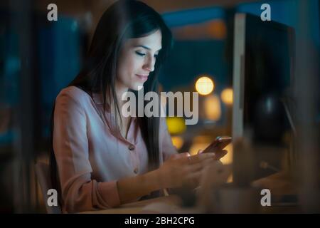 Young woman sitting at desk in office looking at smartphone Stock Photo