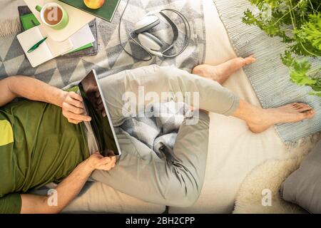 Overhead view of man lying on sofa using tablet Stock Photo