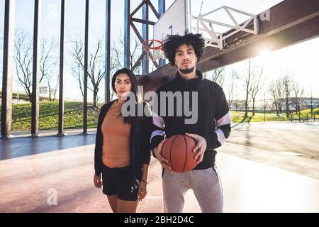 Portrait of young man and woman standing on basketball court in backlight