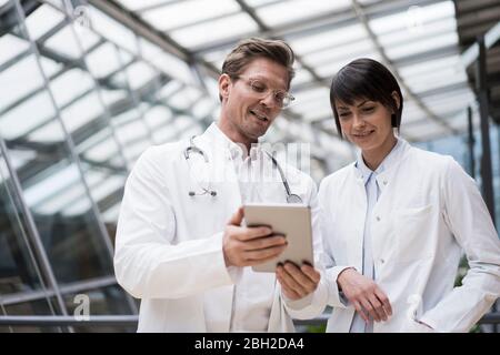 Doctor's standing in atrium, using digital tablet, discussing solutions Stock Photo