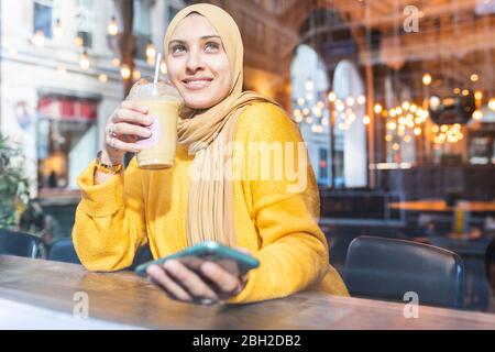 Portrait of young woman with smoothie and smartphone in a cafe Stock Photo