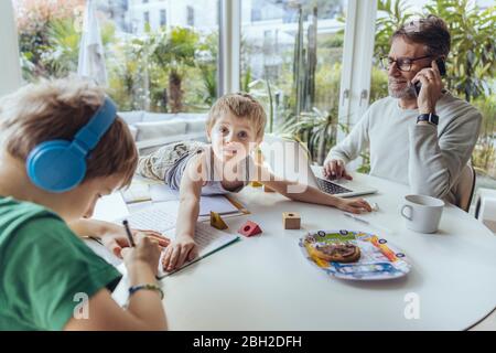 Father talking on the phone while sons are playing on the table Stock Photo