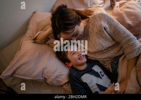 Happy mother and little son lying together on bed having fun Stock Photo