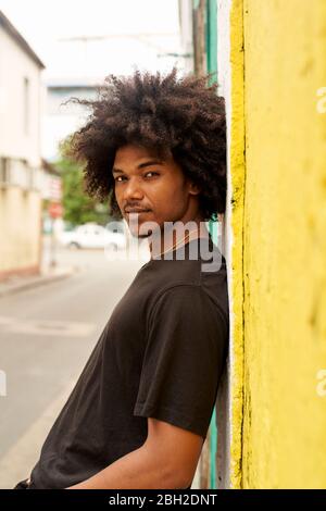 Portrait of young man with afro  leaning against wall Stock Photo