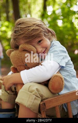 Portrait of boy hugging teddy bear in forest Stock Photo