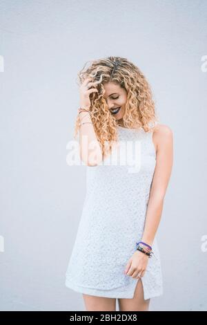 Portrait of smiling young woman with blond ringlets wearing white summer dress Stock Photo