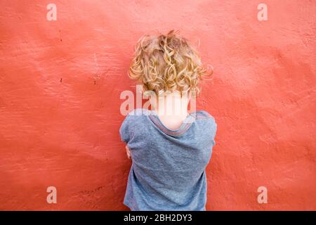 Back view of  little boy standing in front of red wall Stock Photo